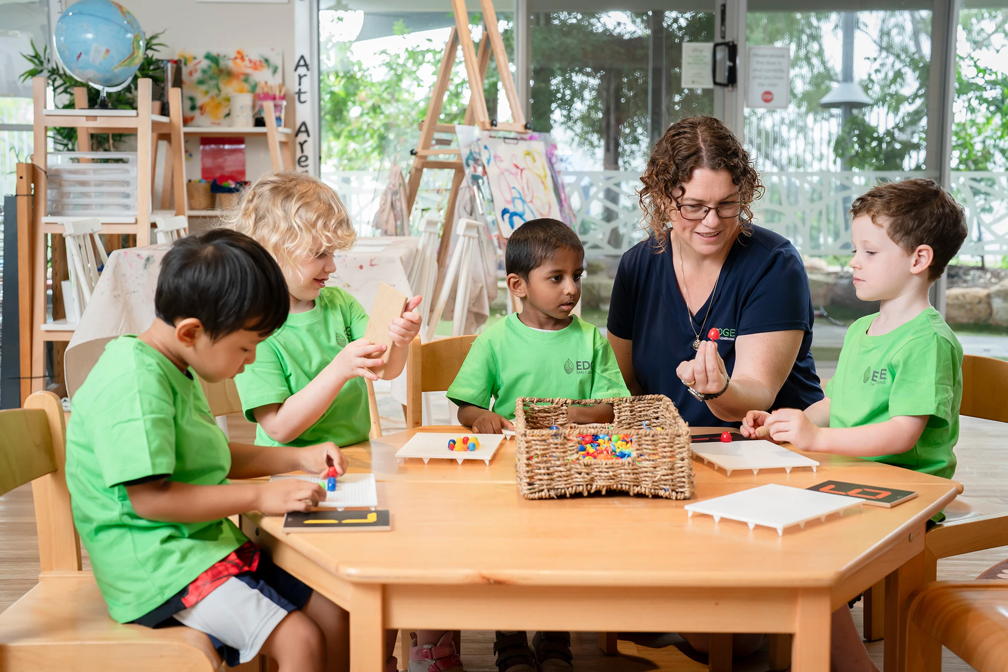 Kindergarten children sitting around a table with a teacher engaging in an activity at a Kelvin Grove daycare centre.