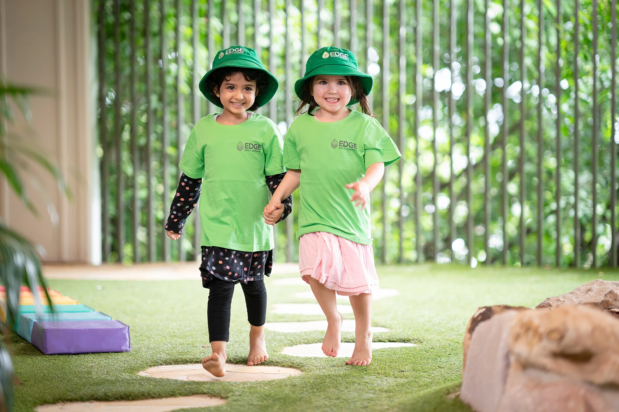 Two kindergarten girls holding hands on stepping stones at Kelvin Grove childcare.