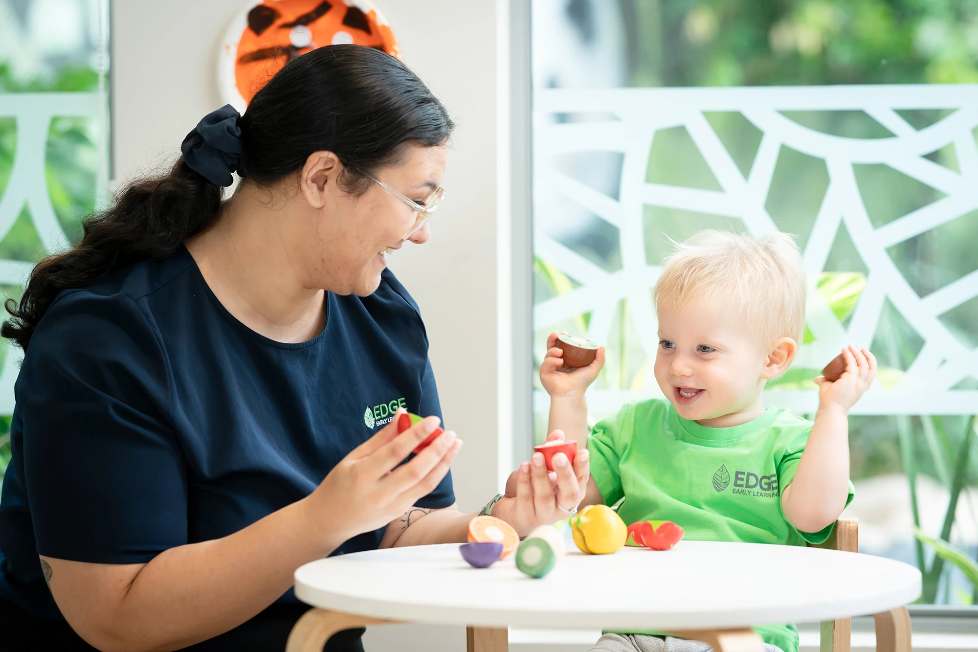Child and early learning educator playing with wooden fruit at Kelvin Grove daycare centre.