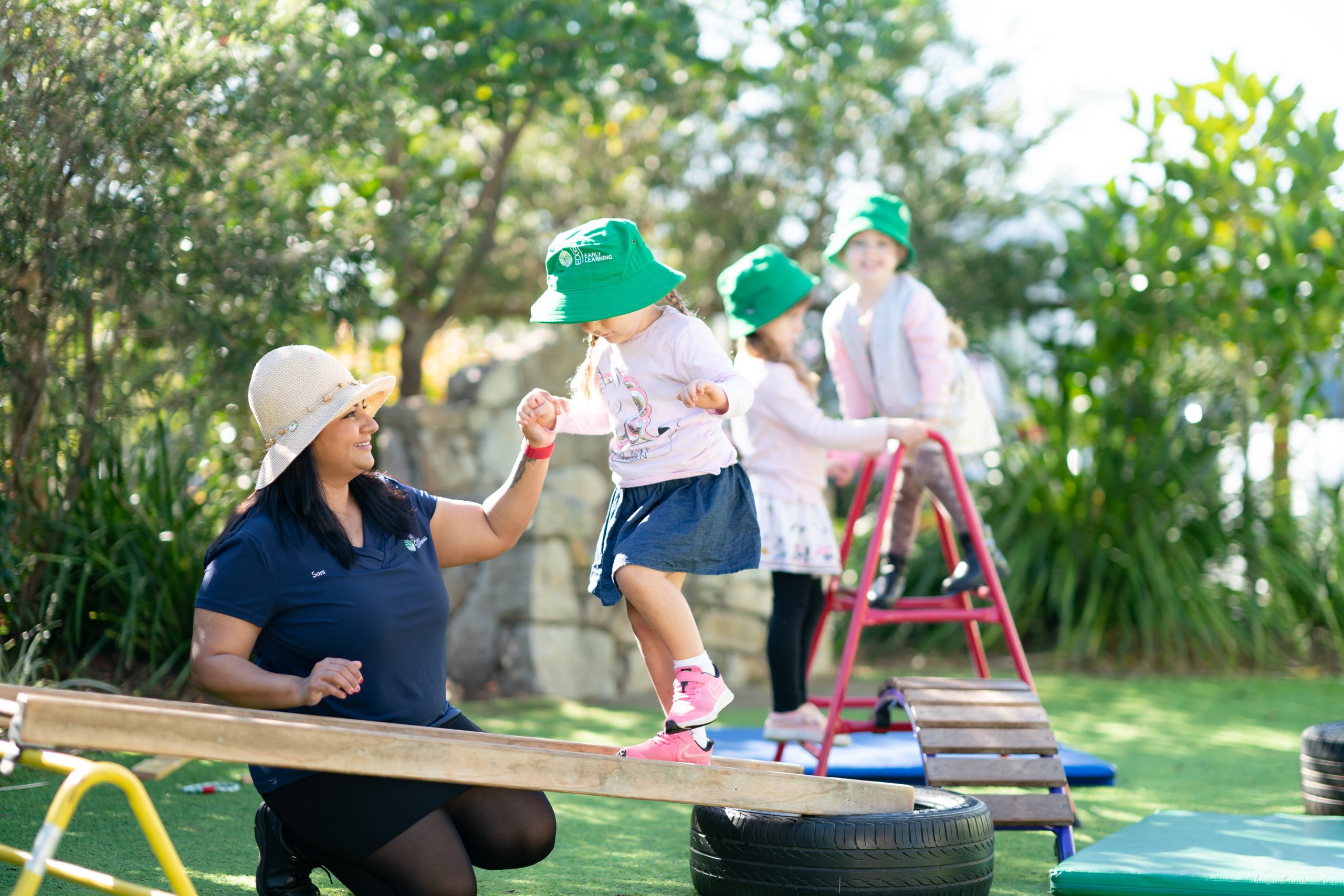 Educator and 2 children joyfully playing together on a colorful playground filled with swings and slides at Edge Maryborough