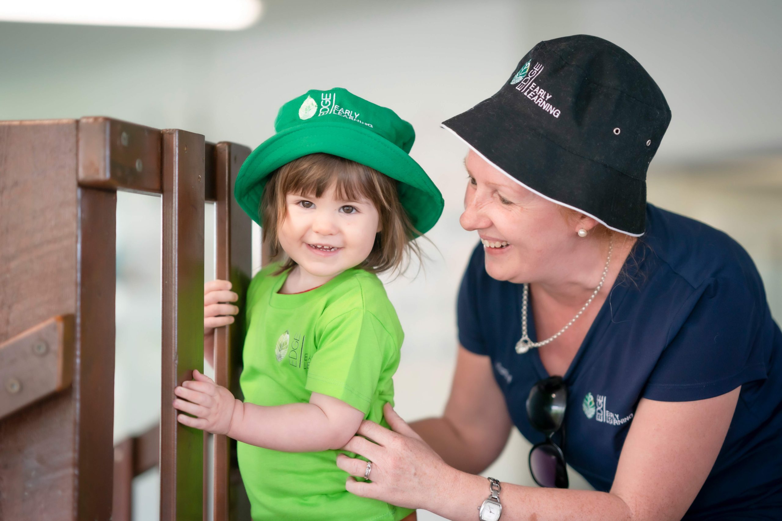 An educator and a child wearing bucket hats, smiling and enjoying a sunny day outdoors at a Laidley childcare