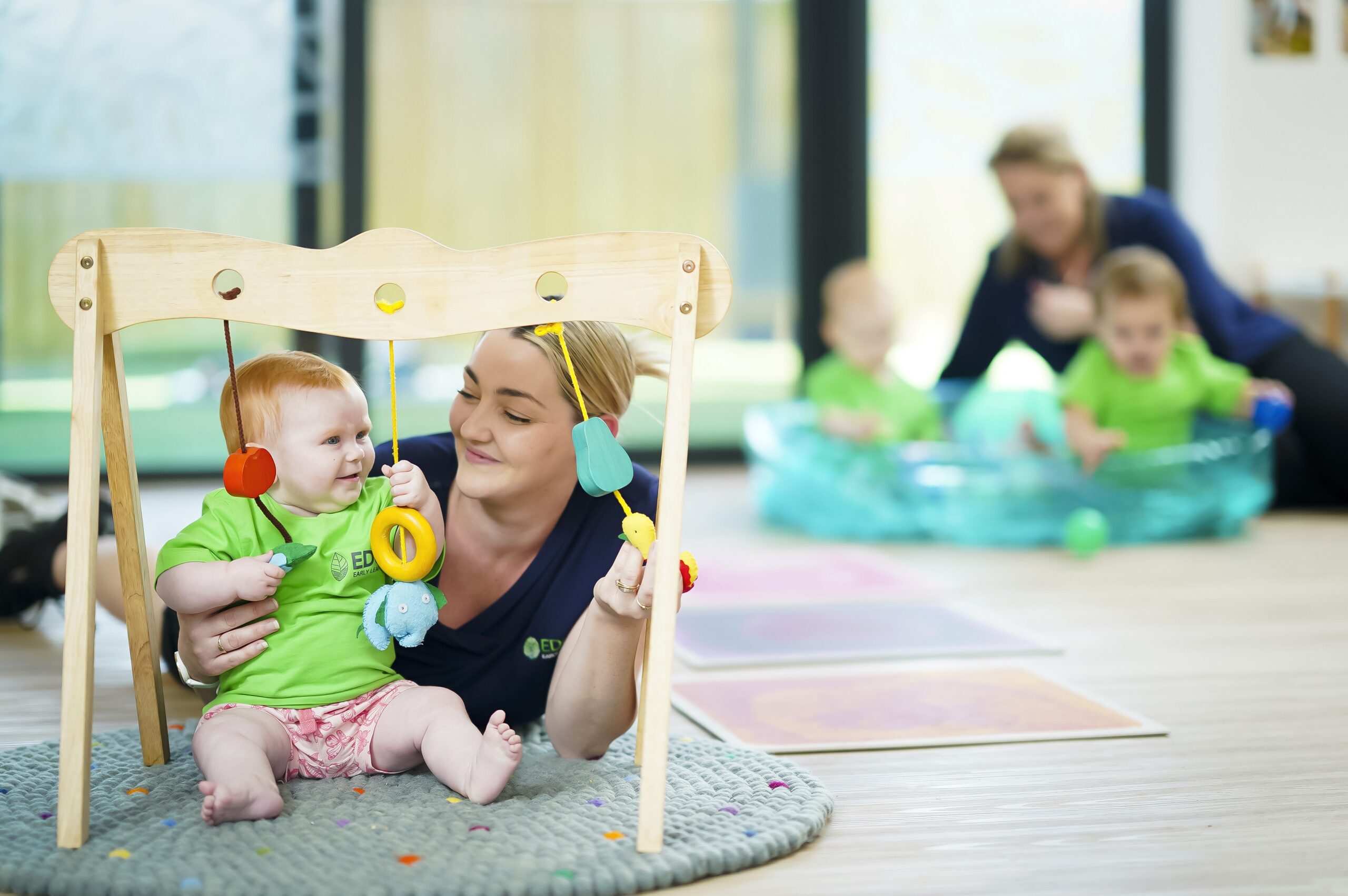 Baby playing with mobile and being supported by an early childhood educator at Edge Early learning Silkstone.