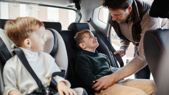 A father fastening his son’s seatbelt in the back seat of a car.