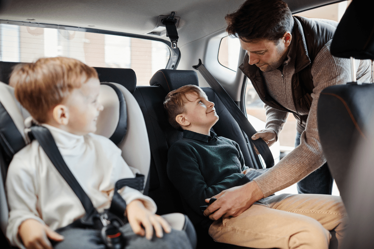 A father fastening his son’s seatbelt in the back seat of a car.