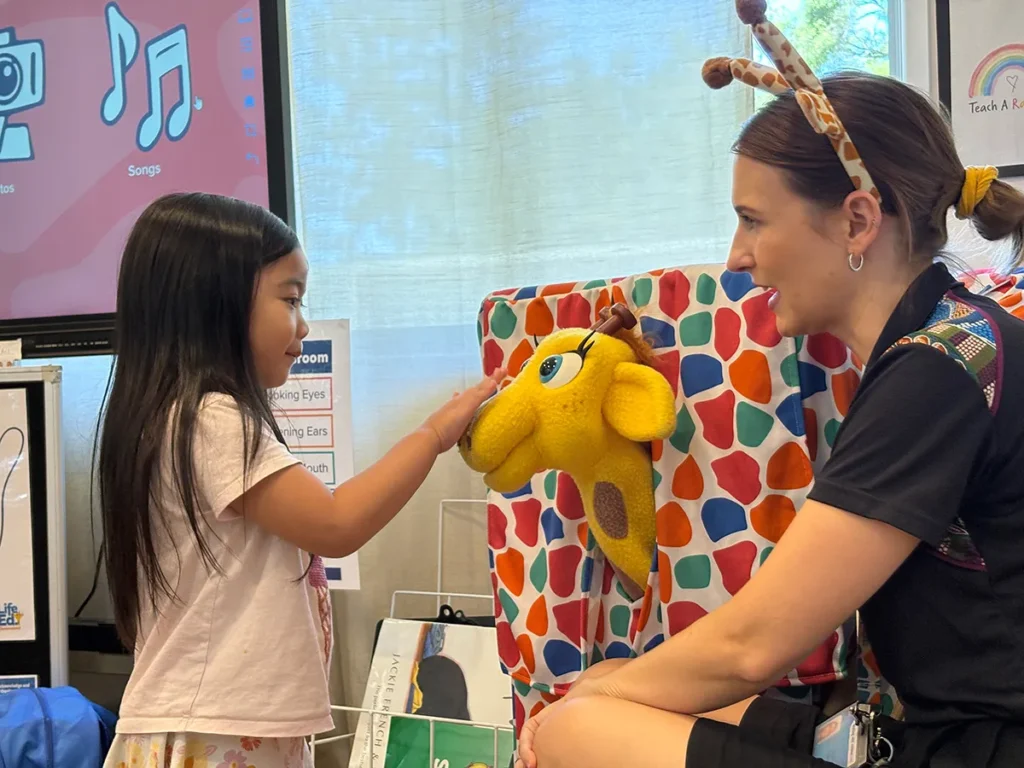 Life Ed's giraffe hand puppet (called Healthy Harold) receiving a pat on the nose from a girl at Edge Early Learning Strathpine.